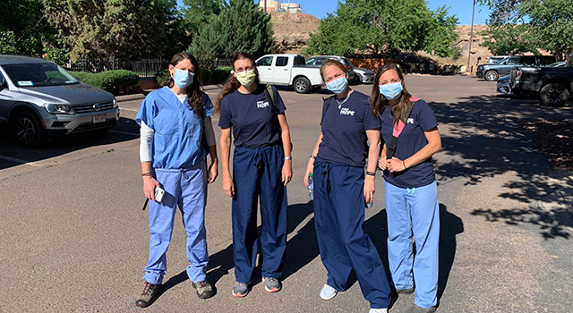 Volunteer medical professionals in blue Project HOPE scrubs and blue medical masks smile and hug in a parking lot of a hospital in the Navajo Nation. 