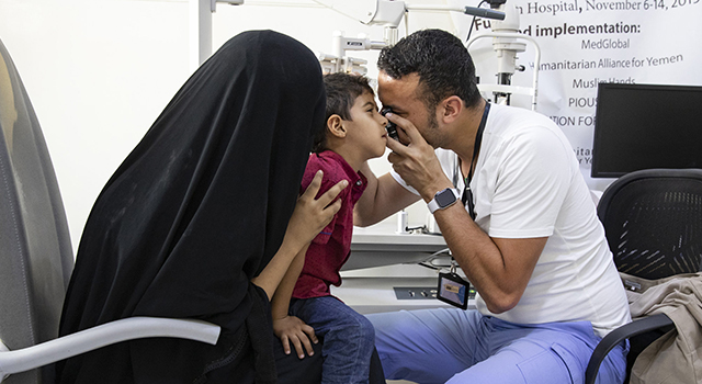 Humanitarian medical teams treat people in  need in Yemen. Here a doctor examines a young boys eyes up close as the boy's mother holds him on her lap.