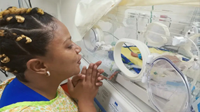 A mother in the Dominican Republic smiles as sits next to her premature baby who is getting treatement in a incubator to grow strong and healthy.