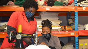 Dorin stitches a mask as a sewing teacher looks on