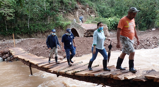 Project HOPE Emergency Medical Team assesses damage in Honduras following Hurricane Eta and Hurricane Iota as they cross a wooden bridge over a swollen river with unstable banks washed away by flooding.