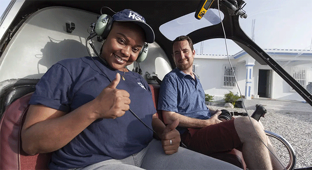 Two Project HOPE emergency responders sit in a helicopter in Haiti. They are smiling and wearing navy Project HOPE polo shirts.