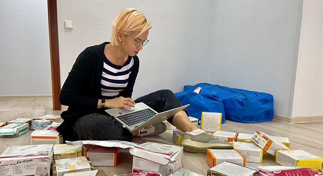 A young blonde woman is looking at a computer as she sits on the floor surrounded by medical supplies.