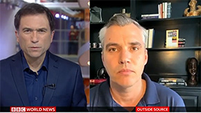 A screenshot of a recent video clip of a BBC World News Interview with Chris Skopec. On the split screen, both men wear navy shirts and look intently at the camera.