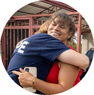 A Ukrainian woman hugs a Project HOPE health worker in a navy shirt as she holds her cellphone with a tan case. She is smiling.