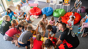 A photo of a safe space for children and families in Poland, showing a group of children with two teachers against a background of brightly-colored bean bags.