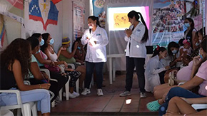 Two Project HOPE-supported health workers in Colombia use a flash light as they speak to a waiting room of pregnant people in need of care after leaving Venezuela.