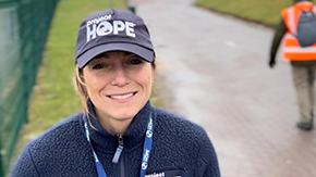 A photo of Chessa Lafiti, wearing Project HOPE hat, lanyard and fleece as she smiles at the camera against the backdrop of a brick path.