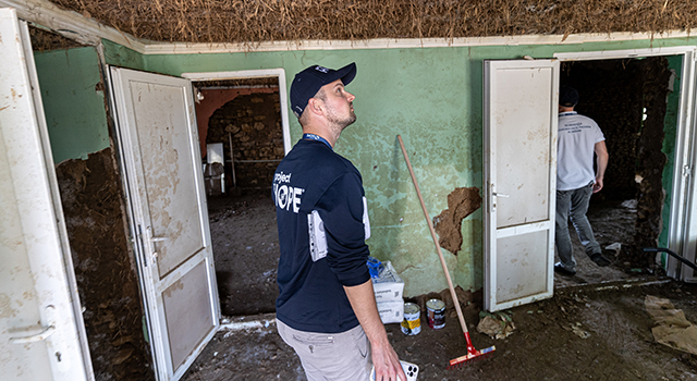 A photograph of a Project HOPE team member looking up at a moldy ceiling covered in brown moss. He is in a room that has been damaged by the flooding after a dam was destroyed in Kherson.