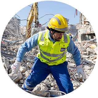 A photograph of a Project HOPE team member wearing safety gear and helmet as they work through the remains of buildings looking for survivors of the February 2023 earthquakes in Turkiye.