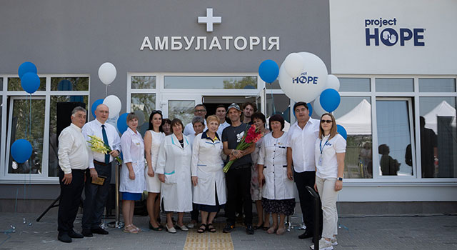 A photograph of a group of health workers and administrators with balloons posing in front of a newly built health clinic.