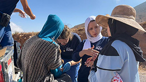 A photograph of Project HOPE partners in Morocco in a group talking to an earthquake survivor sitting in the bed of a truck.