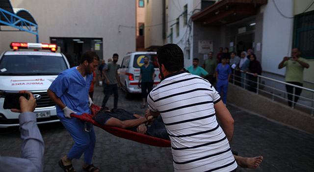 A photograph from Gaza shows two people carrying an injured man on a small stretcher on a street crowded with ambulances and health workers waiting to help.