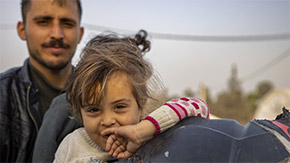 A photograph of young child wearing a sweater and smiling as she holds her hand up to her face in Turkey.