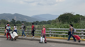 A photograph of people pulling rolling bags and suitcases on a concrete road as they walk to cross the border between Colombia and Venezuela.