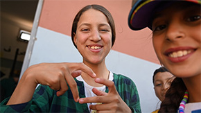 A photograph of two young girls smiling at the camera as one holds up her hands making the shape of a heart in Morocco.