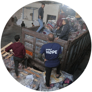 Round photo of a people in Gaza unloading plastic bags of heavy winter blankets from a large, rusty truck bed in a warehouse.