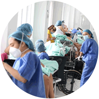 Round photo of a maternity ward in Colombia showing a hallway filled with healthcare workers in scrubs, hair coverings and masks caring for women sitting in wheelchairs and laying in hospital beds.