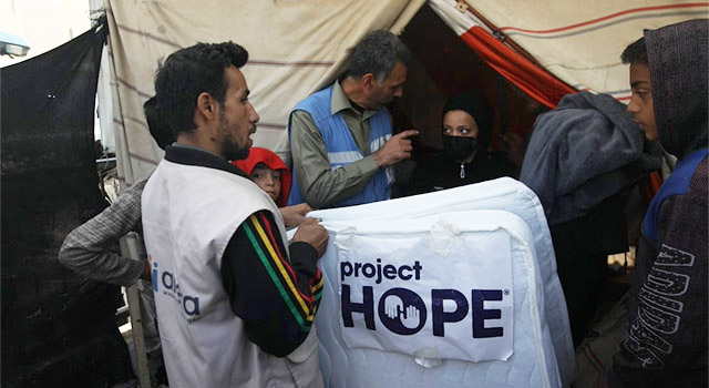 A photograph of Project HOPE partner in Gaza distributing mattresses to a family wearing sweatshirts against the backdrop of a canvas tent.