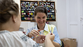 A photograph of Irina, a refugee in Ukraine, as she leads a jewelry-making class for women at Casa Marioarei, one of Project HOPE’s partners in Moldova. She is smiling widely as she helps a student with a delicate bracelet.