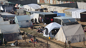 A photograph of tents in Gaza where families displaced by violence have been forced to live. There are bikes scattered around, clothes drying on a line and children playing outside.