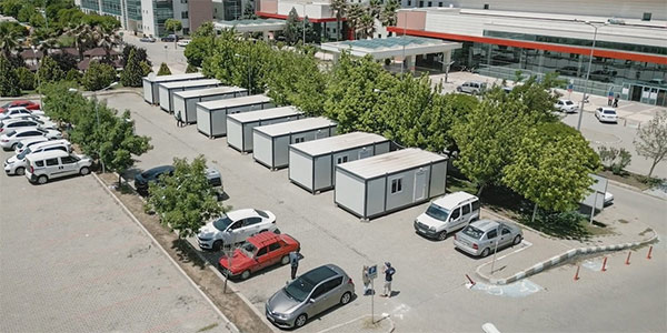 A photograph from Turkiye shows a parking lot with trees and cars, and eight white painted trailers.