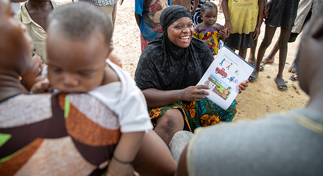 A Project HOPE community health workers smiles at families listening to her and looking at illustrations of health information