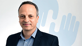 Project HOPE CEO Rabih Torbay is pictured smiling in a dark suit and light blue shirt, in front of two semi-transparent light blue hands from the Project HOPE logo.