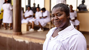 A photograph of a large group of people in Haiti waiting for health care services in a large white room with an open wood beam roof.