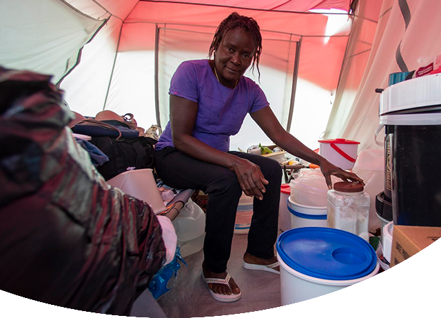 Veronique wears a purple shirt and black pants as she sits in a small white and orange tent which serves as temporary shelter outside homes that were destroyed during Hurricane Dorian in the Bahamas.