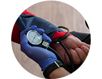 A photograph of a health worker's hand and watch as they take the blood pressure of a person with their arm out and palm closed.