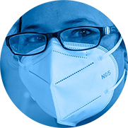 A photograph in the shape of a circle shows a woman girl in India smiling at the camera with her eyes. She is wearing glasses and a white N95 mask that covers her nose and mouth. The photo has a bright blue toned overlay.