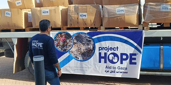 Photograph from Egypt shows a truck bed topped by rows of boxes of hygiene kits labeled with Project HOPE logo. A team member stands in front waiting for the truck to unload.