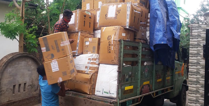 A green truck is filled to the brim with cardboard boxes of supplies. Two men are loading the final boxes of supplies from Project HOPE.