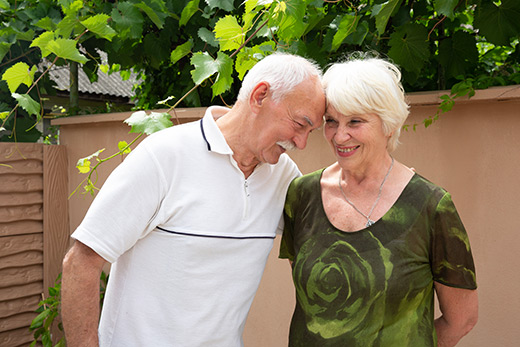 A photo of two senior refugees from the Ukraine conflict at a Project-HOPE supported community center. They are sweetly touching foreheads against the background of a garden wall and many plants.