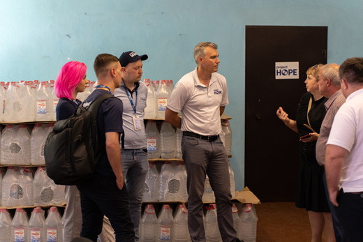 A photo of Chris Skopec speaking with Project HOPE teams in Ukraine against the background of a blue room filled with bottles of water.