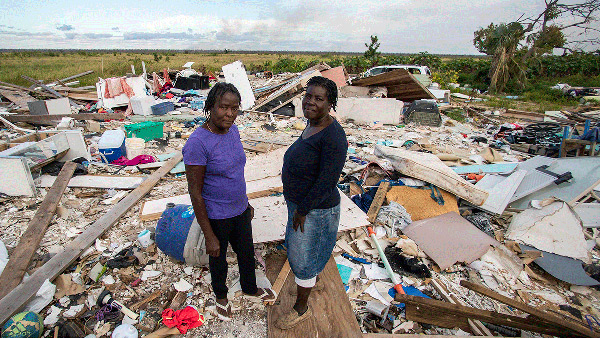 Two women in the Bahamas hug in front of the remains of their home.