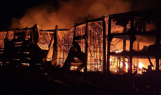 Photograph of a burning warehouse in Ukraine at night. The walls and inner structure are falling down, little of the exterior stands.