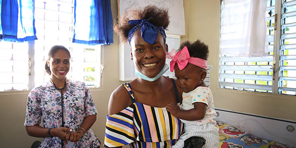 Photograph of a mother holding her small baby, both wear colorful bows in their hair as they stand up to leave a clinic where they were getting care from a health worker in Colombia, supported by Project HOPE.