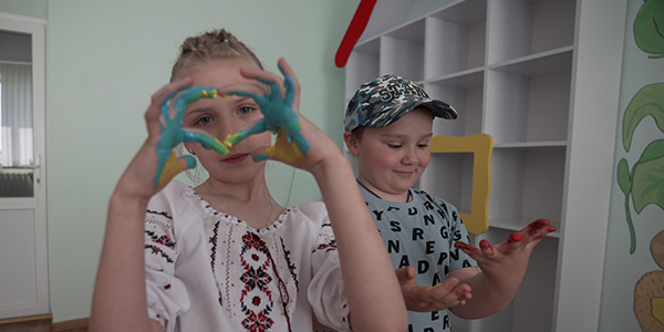 Photograph from Ukraine shows two young children holding up their finger covered with paint at a Project HOPE supported safe space for displaced families to participate in activities and find community. 