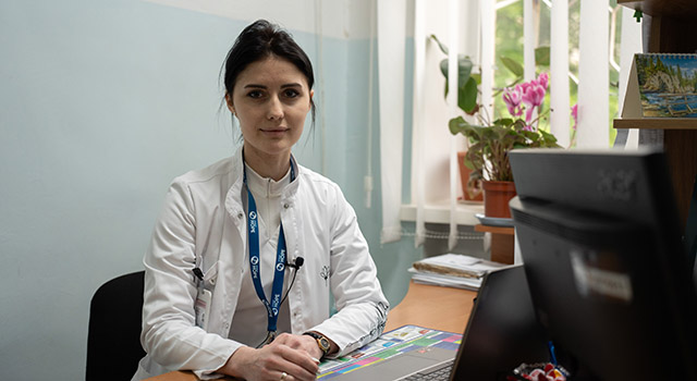 A photograph of Project HOPE health worker in Ukraine as they sit at a desk with a laptop in front of her. She wears a labcoat and Project HOPE lanyard.