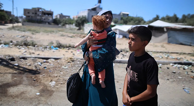 A photograph of a mother and her two children in Gaza walking and looking for safety as they are displaced by violence.