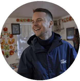 A photograph of Artem an information officer in Ukraine where he is laughing and looking to the left. He wears a turtleneck sweater and Project HOPE rain jacket.