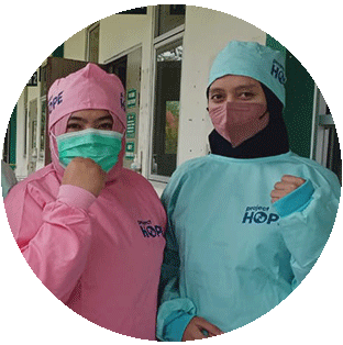 A photograph showing two health workers in Indonesia as they look at the camera and hold up their fists in a gesture of strength. They wear medical masks and Project HOPE scrubs against the background of a hospital.