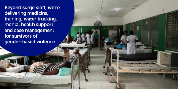 Photograph from inside a hospital in Haiti showing groups of nurses in uniforms talking to each other and patients, alongside people lying in basic metal beds.